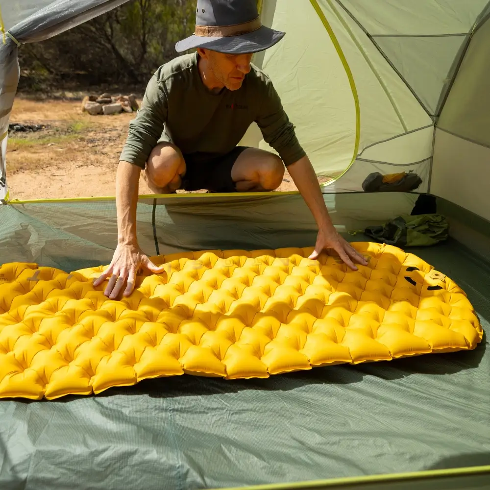 Person in a tent setting up a yellow Ultralight XR Insulated Air Isomatte, ideal for motorcycle camping.
