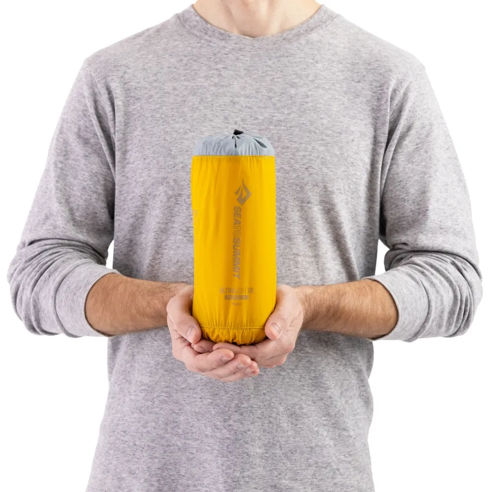 Person hält eine kompakte, gelb verpackte Ultralight XR Insulated Air Isomatte in den Händen, ideal für Motorrad-Camping.