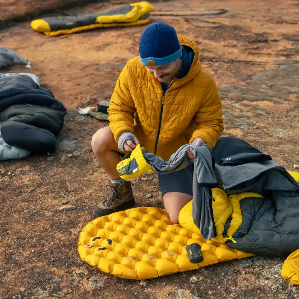 Ein Camper mit gelber Isomatte und Schlafsack beim Motorrad-Camping in felsigem Gelände. Ideal für Outdoor-Abenteuer.