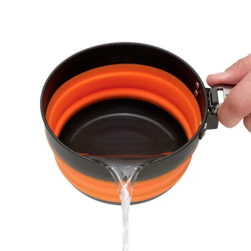 Ein zusammenklappbarer Camping-Kochtopf aus einem 3-teiligen Kochset, mit einem leuchtend orangefarbenen, flexiblen Körper und einem schwarzen Rand, aus dem Wasser gegossen wird. Ideal für Motorrad-Camping.