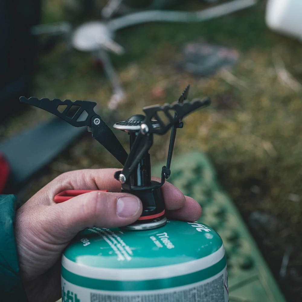 Nahaufnahme eines kompakten Gaskochers, der von einer Hand gehalten wird, ideal für Motorrad-Camping.