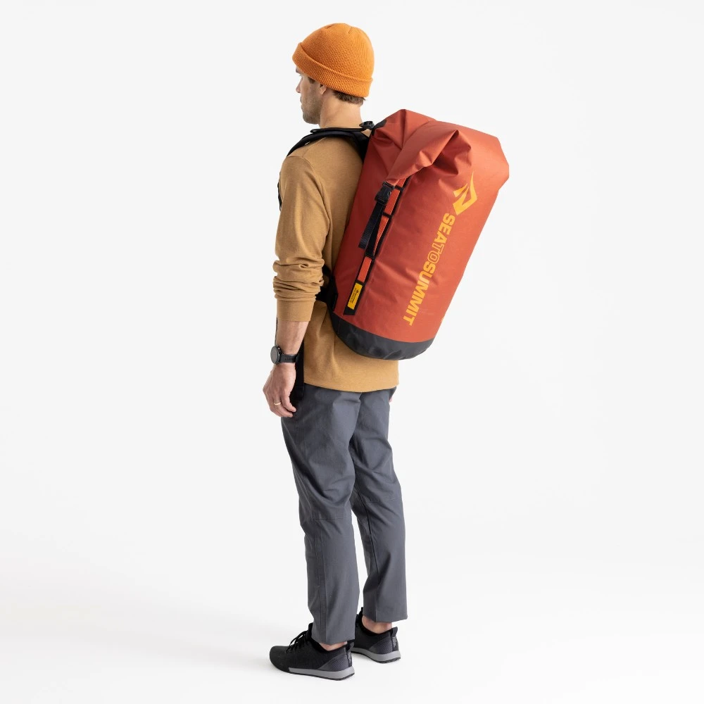 Mann mit orangefarbener Big River Dry Backpack 50 Liter von Sea to Summit, geeignet für Motorrad-Camping und Outdoor-Abenteuer.