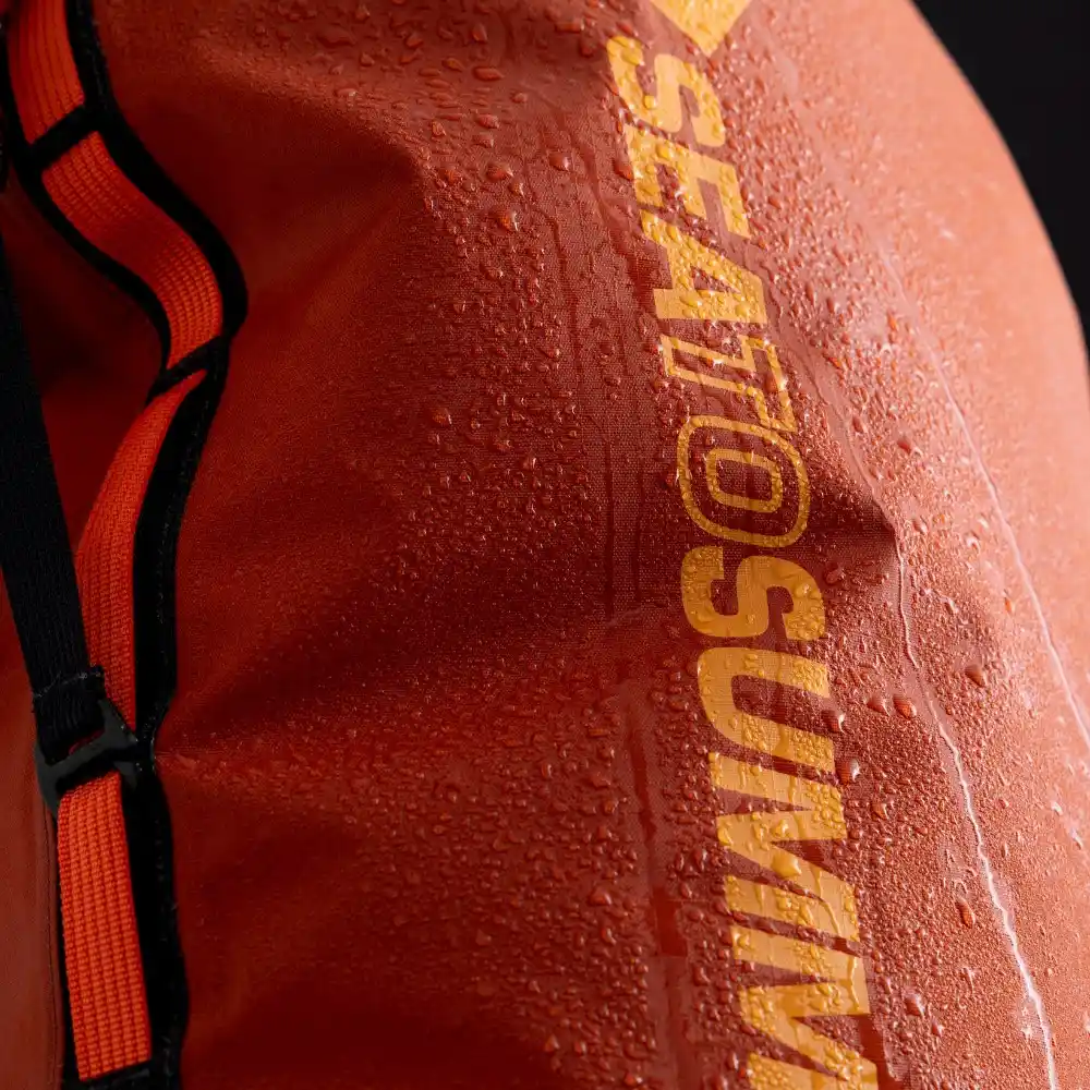 Nahaufnahme eines orangefarbenen Big River Dry Backpacks von Sea to Summit mit Wassertropfen darauf, ideal für Motorrad-Camping.
