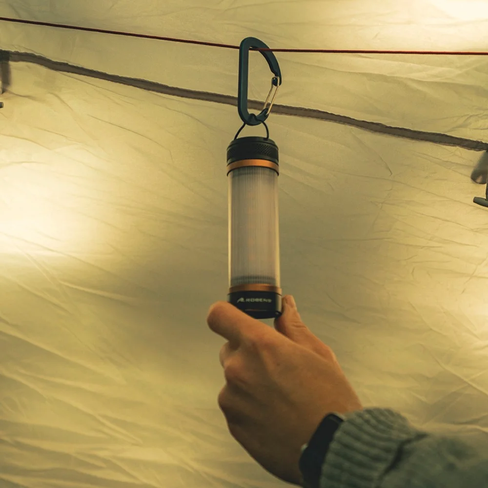 Eine Hand hält die 3in1 Taschenlampe Arran, die mit einem Karabiner an einer Zeltschnur hängt. Ideal für Motorrad-Camping-Abenteuer.